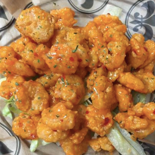 A plate of orange-glazed shrimp on a bed of lettuce, garnished with herbs.