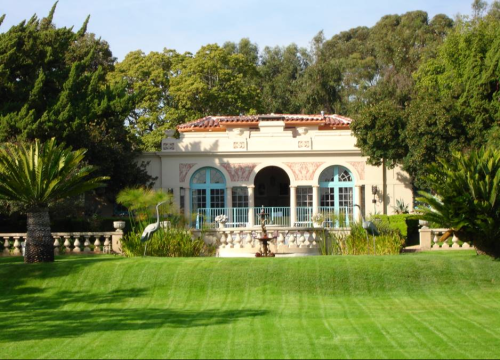 A charming house with blue accents surrounded by lush greenery and palm trees, set in a well-maintained garden.