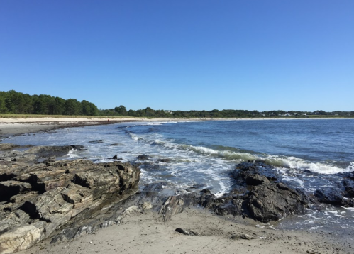 A serene beach scene with rocky shorelines, gentle waves, and clear blue skies in the background.