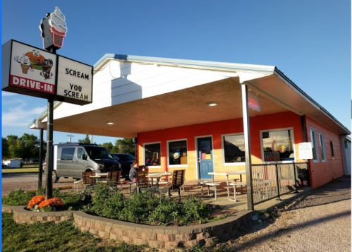 A colorful drive-in ice cream shop with outdoor seating and a sign that says "Scream You Scream." Clear blue sky above.