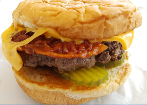 Close-up of a cheeseburger with bacon, pickles, and melted cheese on a toasted bun.