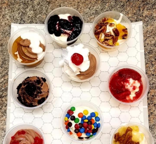 A variety of dessert cups with toppings like whipped cream, fruit, nuts, and candies arranged on a tray.