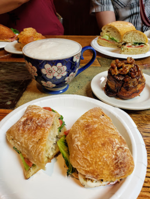 A plate with a sandwich, a cup of frothy coffee, and various pastries on a table.