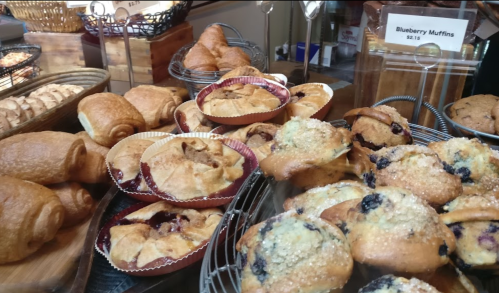 A display of assorted baked goods, including croissants and blueberry muffins, in a bakery setting.