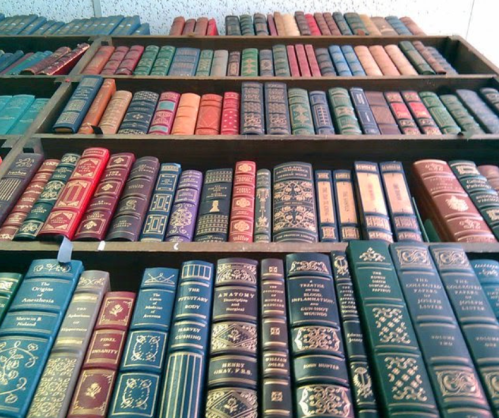 A close-up of a bookshelf filled with colorful, ornate leather-bound books arranged neatly on wooden shelves.