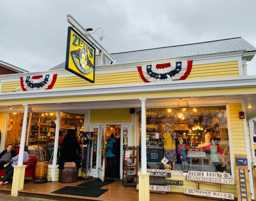 A colorful storefront with a sign reading "Zee's" and patriotic decorations, featuring people inside and outside.