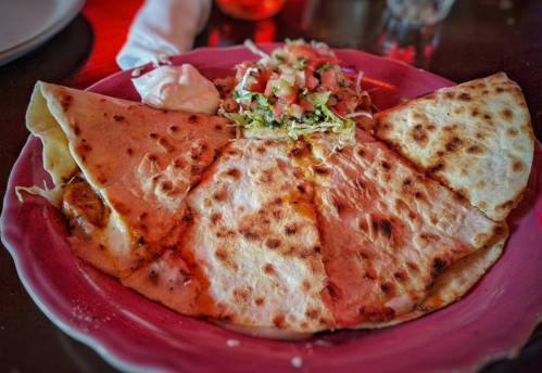 A plate of quesadillas with melted cheese, served with a side of salad and sour cream.