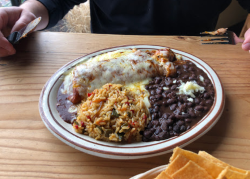A plate of enchiladas topped with cheese, served with rice, black beans, and tortilla chips on a wooden table.