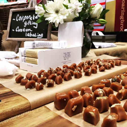 A display of caramel candies and gift packaging options on a table, with flowers and a sign about corporate gifting.