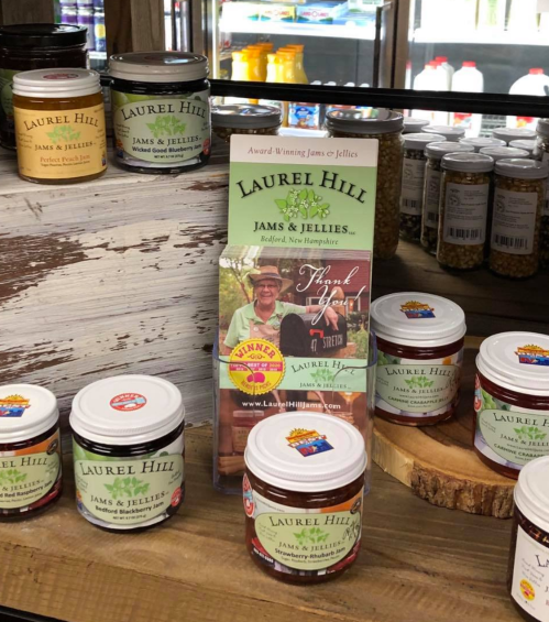 Display of Laurel Hill Jams & Jellies jars with a promotional brochure on a wooden shelf.