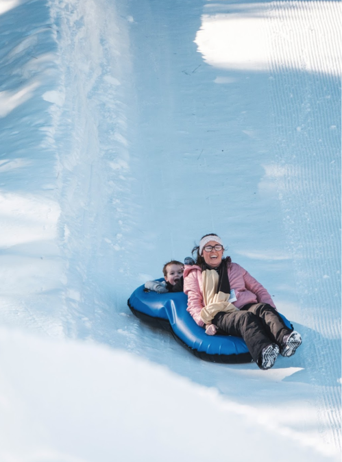 Two people joyfully sledding down a snowy slope on a blue inflatable tube.