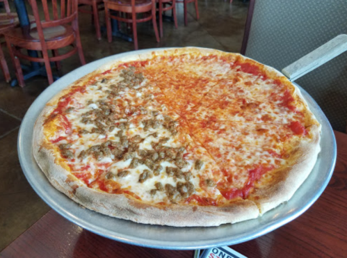 A large pizza on a metal tray, half topped with cheese and tomato sauce, half with cheese and ground meat.