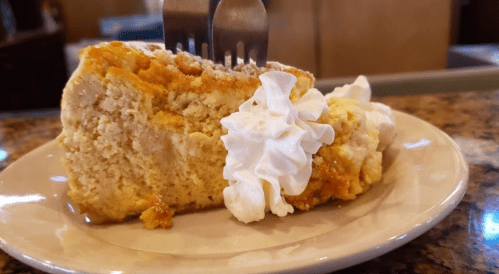 A slice of cake topped with whipped cream, served on a plate with two forks inserted into the cake.