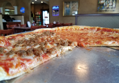 A close-up of a pizza with one half topped with cheese and the other half with meat, set in a restaurant interior.