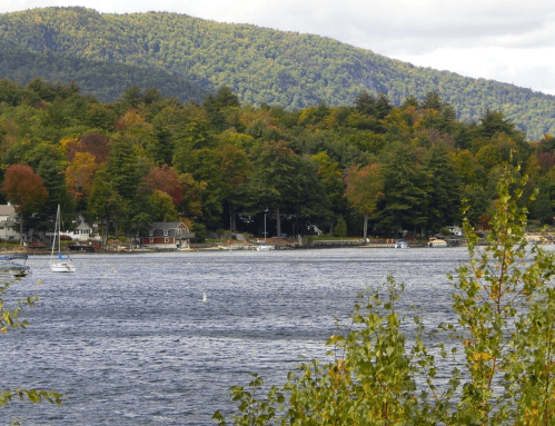 A serene lake scene with boats, surrounded by colorful autumn trees and mountains in the background.