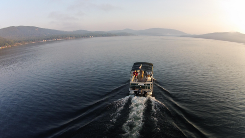A boat glides across a calm lake at sunrise, surrounded by mountains and a serene landscape.