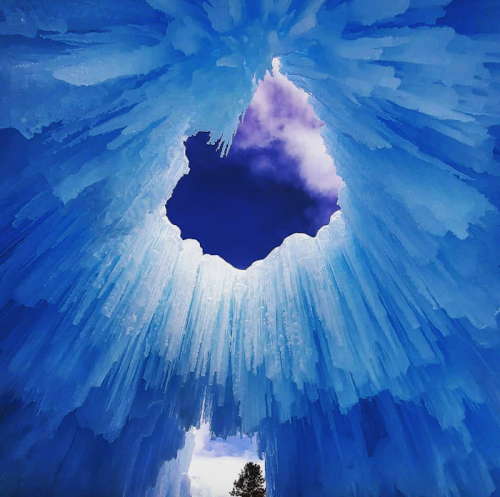 View from below an ice cave, featuring striking blue icicles and a heart-shaped opening revealing a purple sky.