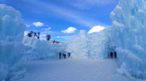 A winter scene featuring towering blue ice formations and visitors exploring a snowy landscape under a bright sky.