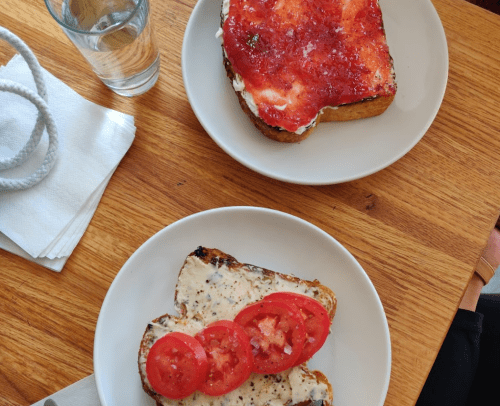 Two plates of toast: one with cream cheese and tomato slices, the other with jam. A glass of water is nearby.