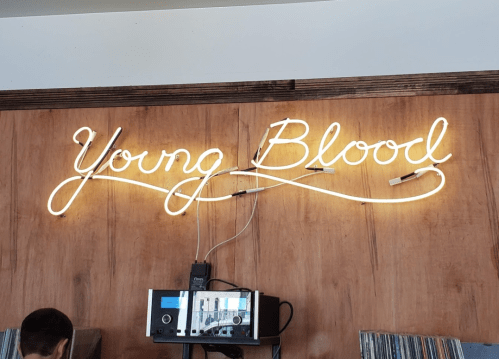 Neon sign reading "Young Blood" on a wooden wall, with a record player visible below.