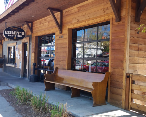 Exterior of Edley's Bar-B-Que featuring a wooden bench and large windows, set in a rustic wooden building.