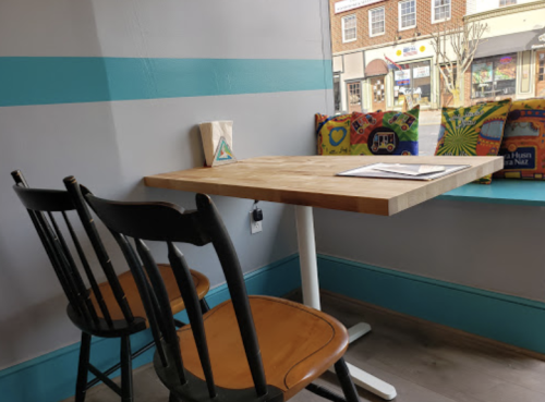A cozy café corner with a wooden table, two chairs, and colorful cushions by the window.