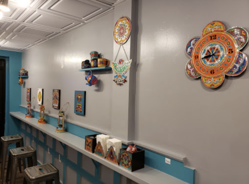 Colorful wall decor featuring traditional art pieces and a clock, with a bar area and stools below.
