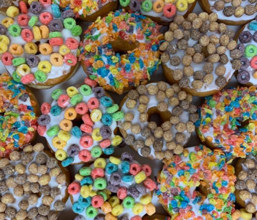 A colorful assortment of donuts topped with cereal, featuring vibrant sprinkles and icing.