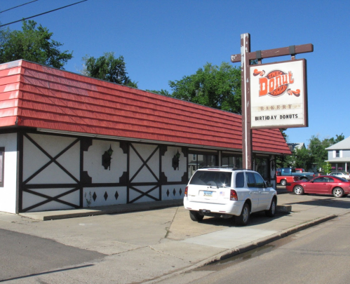 A donut shop with a red roof and a sign reading "Birthday Donuts," parked cars visible in the lot.
