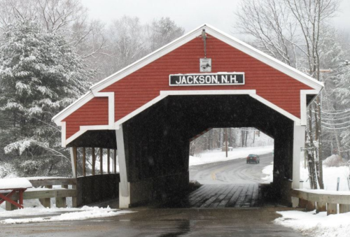 A red covered bridge in Jackson, NH, surrounded by snow-covered trees and a winter landscape.