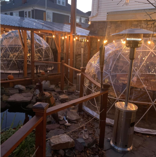 Two transparent igloo-like structures are set up outdoors, surrounded by string lights and a small pond.