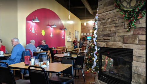 Cozy café interior with stone fireplace, festive decorations, and patrons enjoying meals at wooden tables.