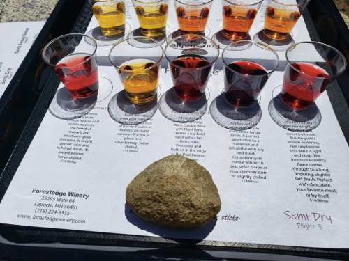 A tray with colorful wine samples and a rock, alongside a menu from Forestedge Winery in Laporte, MN.