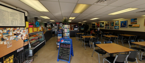 A cozy café interior with tables, a menu board, and colorful artwork on the walls. Customers are seated in the background.