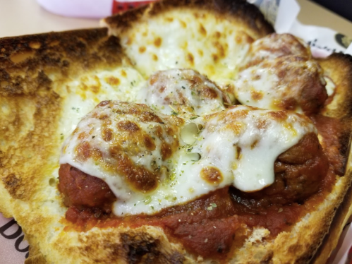 A close-up of a toasted bread slice topped with meatballs, marinara sauce, and melted cheese.