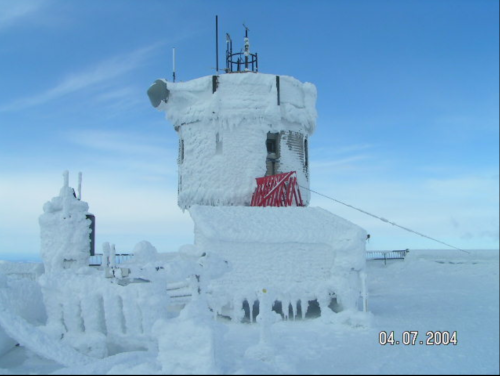 A snow-covered tower with ice formations, set against a blue sky, showcasing extreme winter conditions.