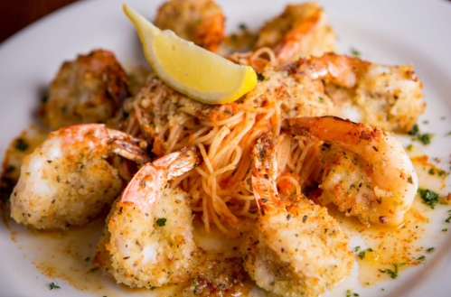 A plate of shrimp scampi with lemon, served over pasta and garnished with herbs.