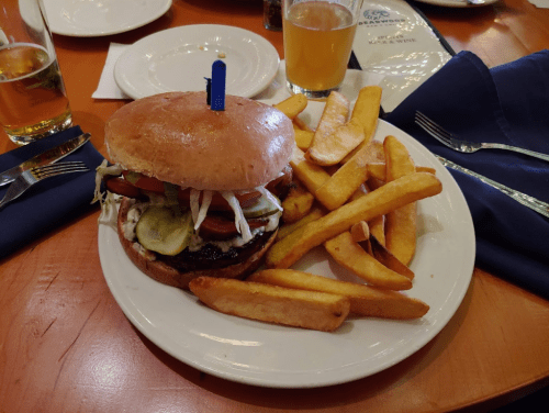 A juicy burger topped with lettuce, tomato, pickles, and fries on a plate, with a drink in the background.
