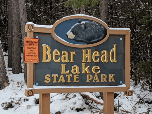 Sign for Bear Head Lake State Park, featuring a bear graphic, with a warning about restricted areas for shooting and hunting.