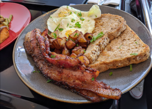 A plate of breakfast featuring eggs, toast, crispy bacon, and seasoned potato cubes, garnished with herbs.