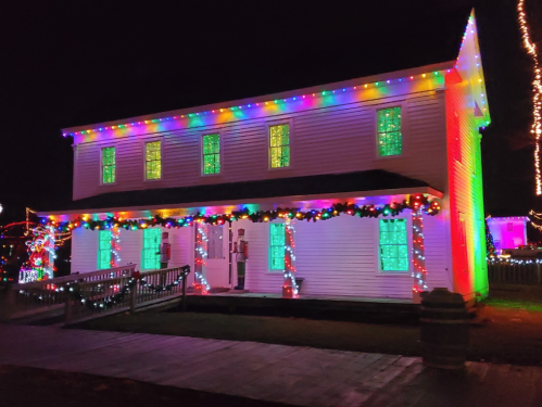 A brightly lit house decorated with colorful Christmas lights and garlands, set against a night sky.
