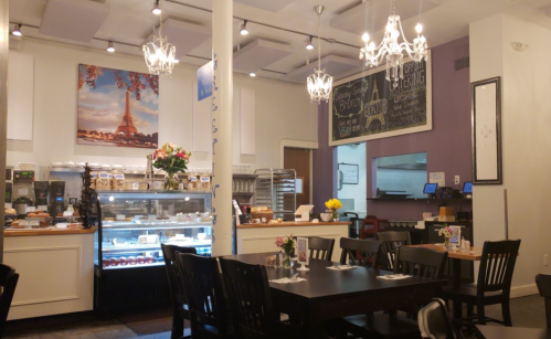 Cozy café interior with elegant chandeliers, a display case of pastries, and tables set for dining.