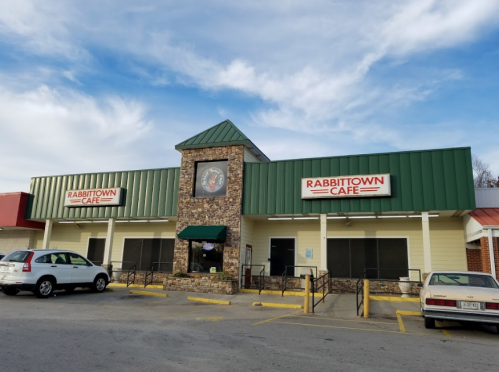 Exterior of Rabbittown Cafe featuring a stone facade and green roof, with a parking area in front.
