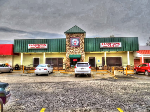 Exterior of Rabbittown Cafe featuring a stone facade and green roof, with parked cars in the lot under a cloudy sky.