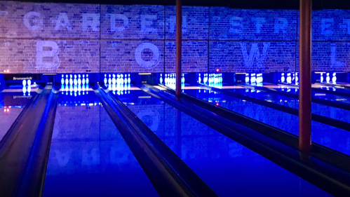 Bowling alley with illuminated lanes and a brick wall displaying "Garden Street Bowl" in blue lighting.