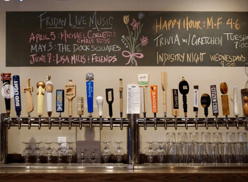 Chalkboard menu with live music dates and a bar featuring various beer taps. Happy hour and trivia details included.