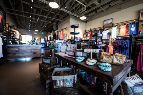 A vibrant retail store interior featuring clothing displays, a wooden table with decor, and colorful merchandise on shelves.