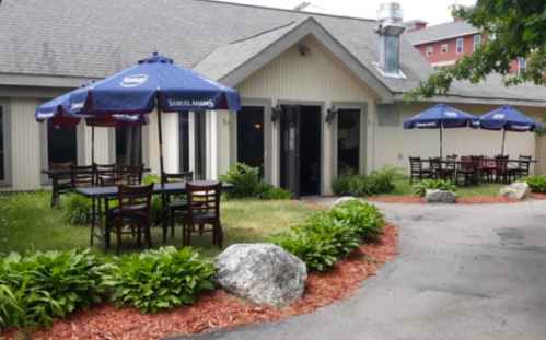 Outdoor seating area of a restaurant with tables under blue umbrellas, surrounded by greenery and decorative rocks.
