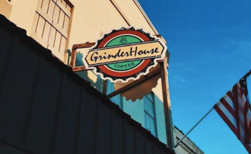 Sign for GrinderHouse Coffee against a blue sky, with an American flag in the foreground.
