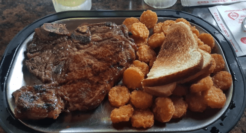 A plate featuring a large steak, golden tater tots, and slices of toasted bread.